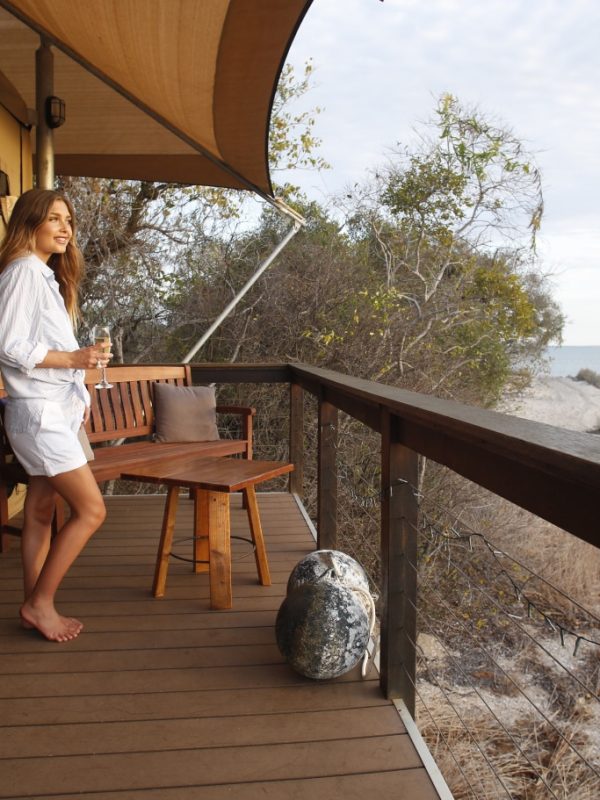 Bayview Safari Tent A girl stands with a glass of wine in hand, admiring the beautiful Cygnet Bay and remote location that surrounds her Glamping Safari Tent in the Diver's Village of Cygnet Bay Pearl Farm.