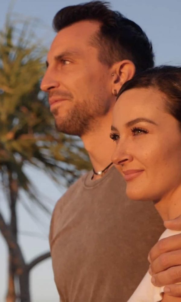 A couple stand side by side watching the sunset of Cygnet Bay, their faces flowing in an orange hue.