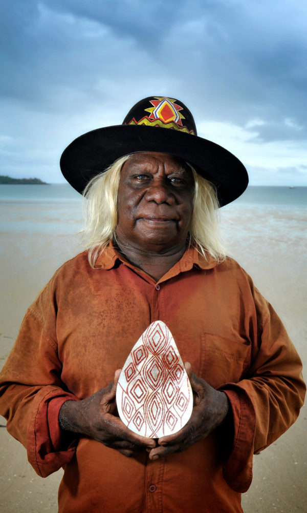 Bruce Wiggan stands on the sands of Cygnet Bay, holding a Riji he himself has designed and carved.