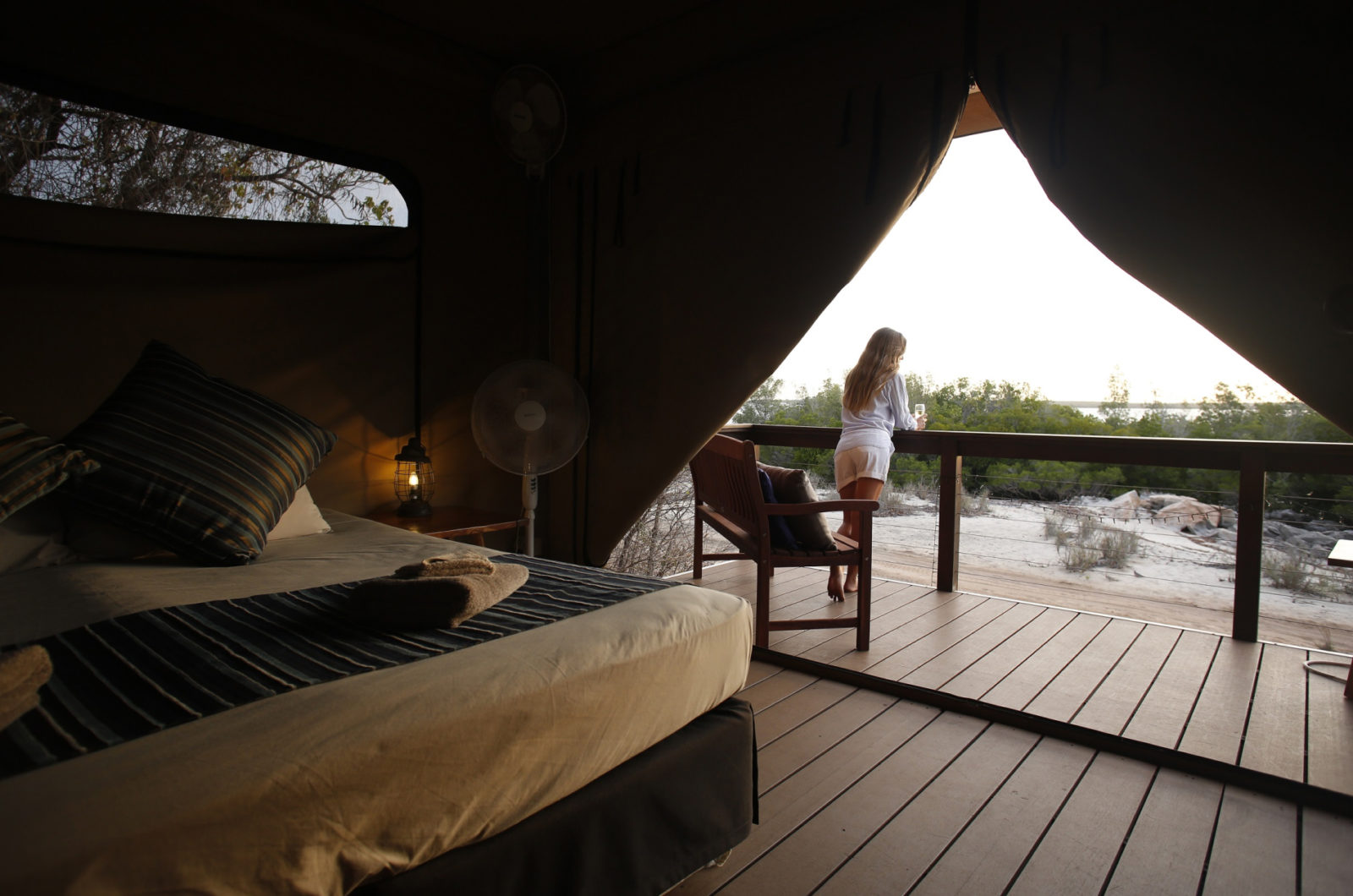 A girl stands with a glass of wine in hand, admiring the beautiful Cygnet Bay and remote location that surrounds her Glamping Safari Tent in the Diver's Village of Cygnet Bay Pearl Farm.