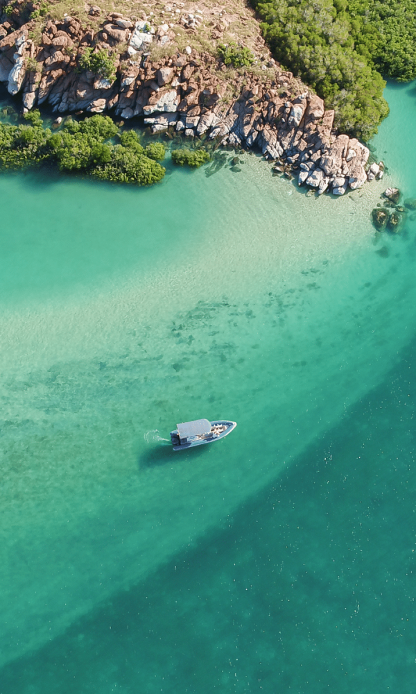 A beautiful aerial visual of a boat dancing across the waves, travelling past the Archipelago Islands that are scattered along the coastline of the Dampier Peninsula, with turquoise blue waters that are almost crystal clear.
