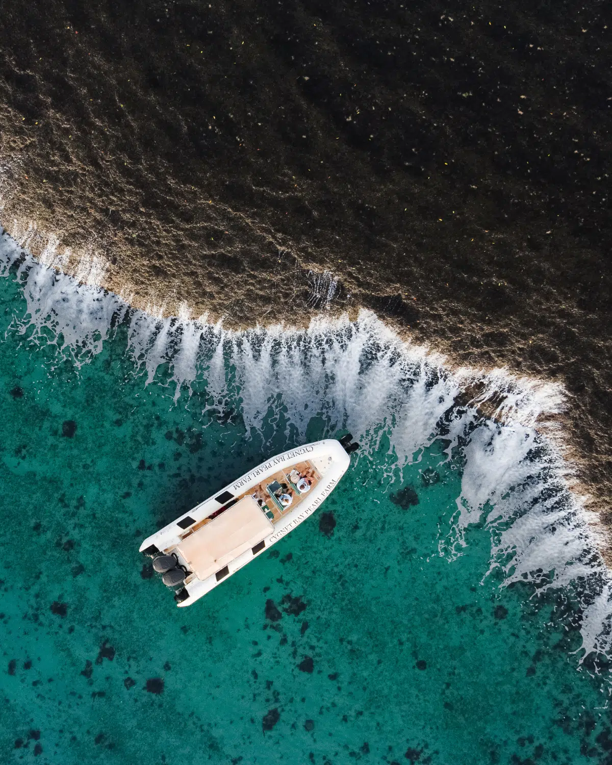 A Cygnet Bay boat sits idly next to the iconic Waterfall Reef, spilling water during the low tide of the ocean. The guests on the boat bare witness to this unique natural phenomenon and are in awe of it's cascading waterfall effect.