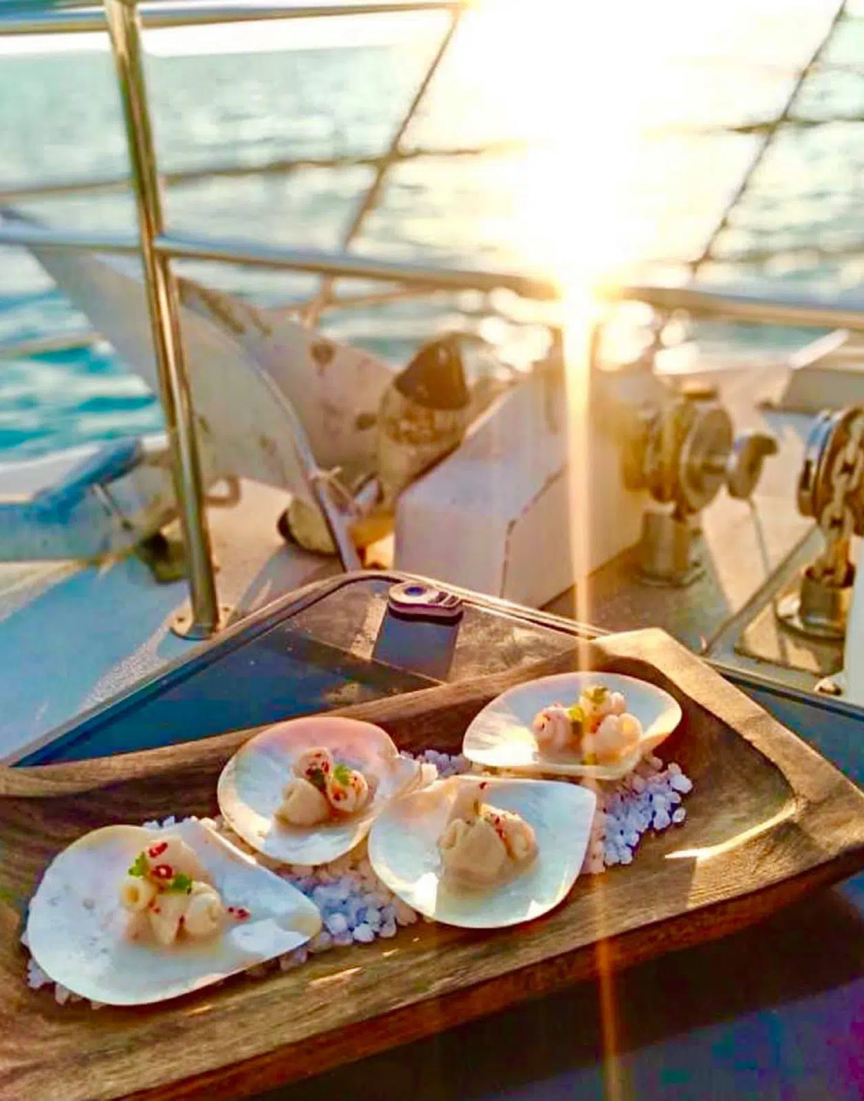 On a boat at sea in Broome is a plate of Australian South Sea pearl meat, elegantly served with micro herbs. In the distance is the beautiful sea with a stunning sunset.