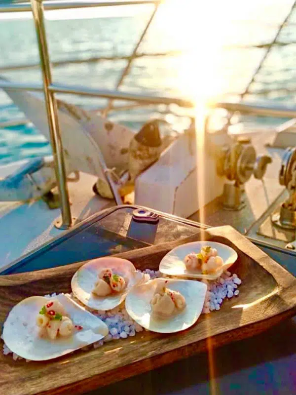 On a boat at sea in Broome is a plate of Australian South Sea pearl meat, elegantly served with micro herbs. In the distance is the beautiful sea with a stunning sunset.