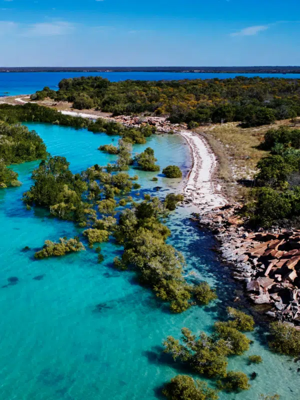 The beautiful turquoise waters of Cygnet Bay meet the white, pristine sands of the Dampier Peninsula, with rocky red terrain scattered on the coastline.
