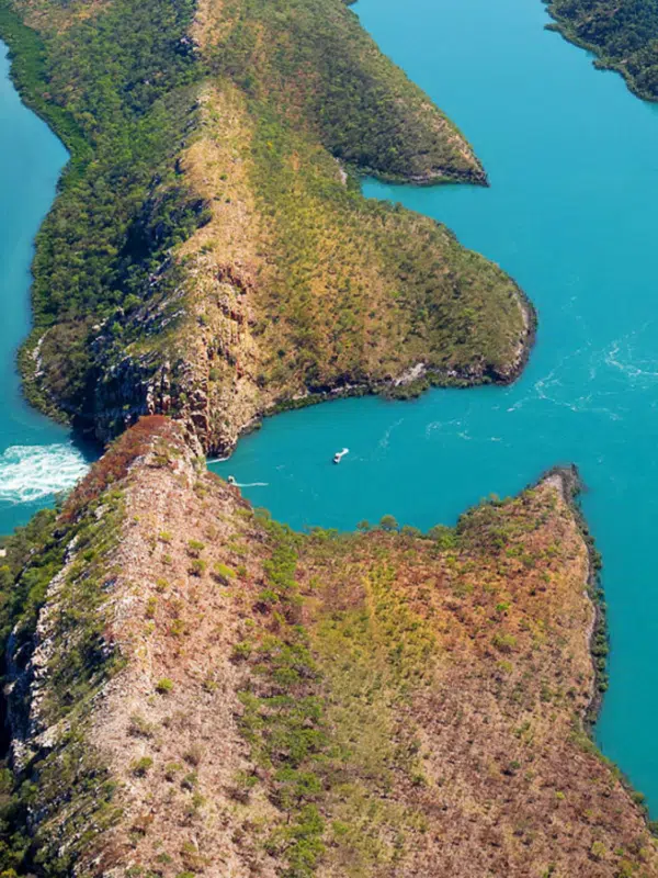 An aerial visual of the intense, rushing waters of the natural phenomenon that is the Horizontal Falls. This marine marvel occurs due to the tides pushing through the two islands, side by side, and produce a 'waterfall' through the landmarks. The sea is turqouise blue, and aside from the tidal waters creating white foaming waves, the rest of the ocean is calm and still.