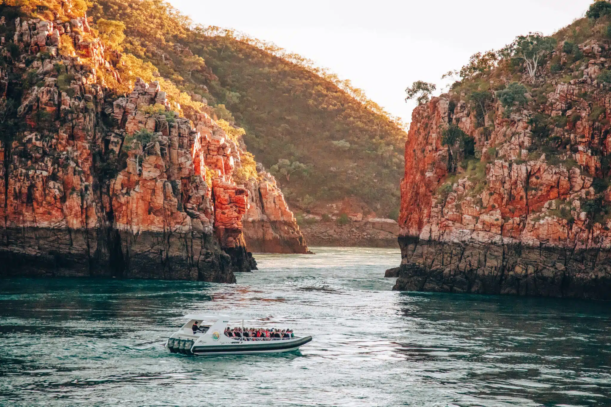 A boat sits on the calm, turqouise waters in the foreground, in front of the iconic Horizontal Falls. The Horizontal Falls are an unusual natural phenomenon on the coast of the Kimberley region in Western Australia, where tidal flows causes waterfalls on the ebb and flow of each tide. Horizontal Falls Soar, Cruise & Overnight Stay.