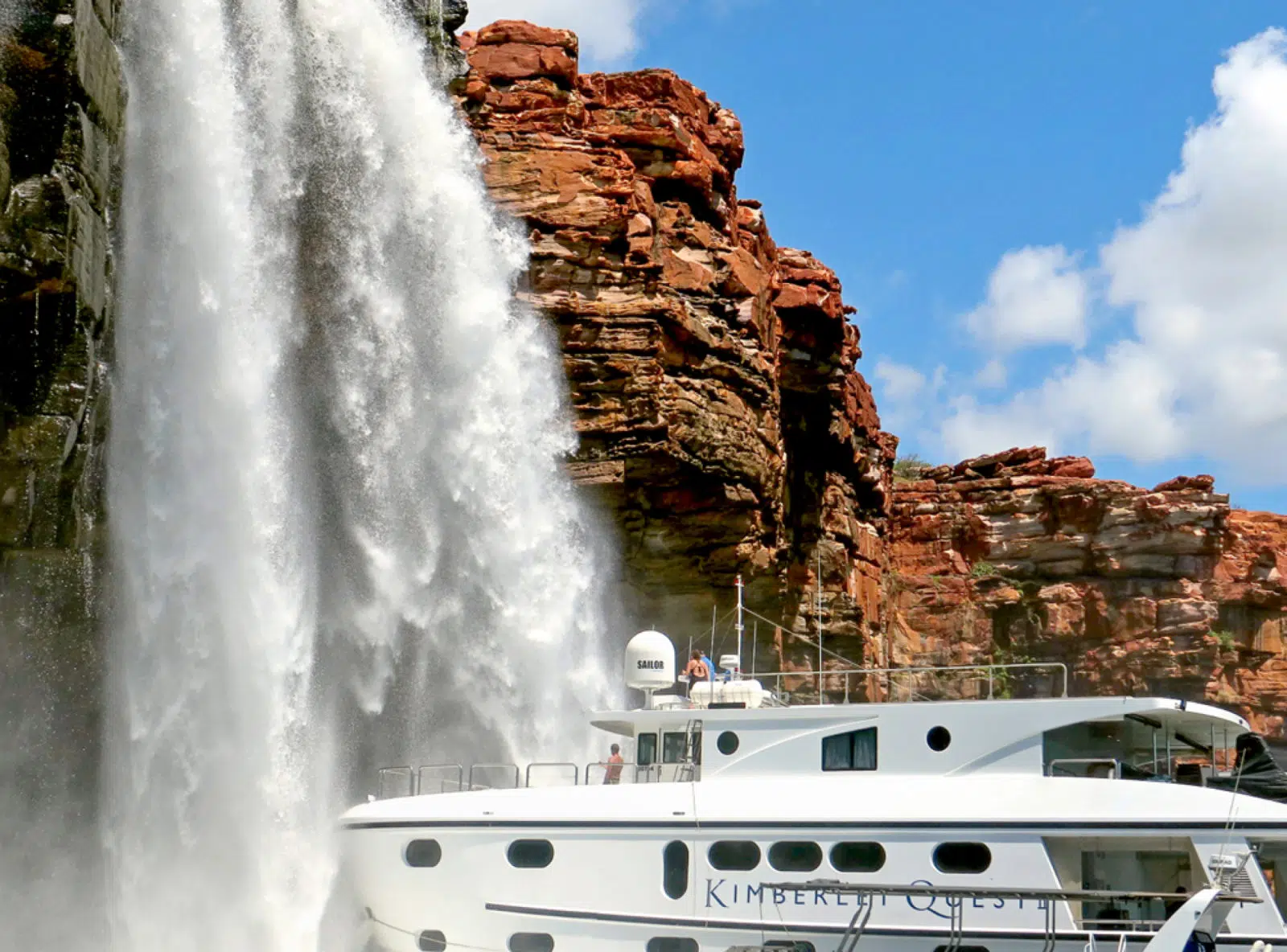 Guests on the Kimberley Quest II are right by Mitchell Falls, enjoying the waterfall cascading from the red cliff face.