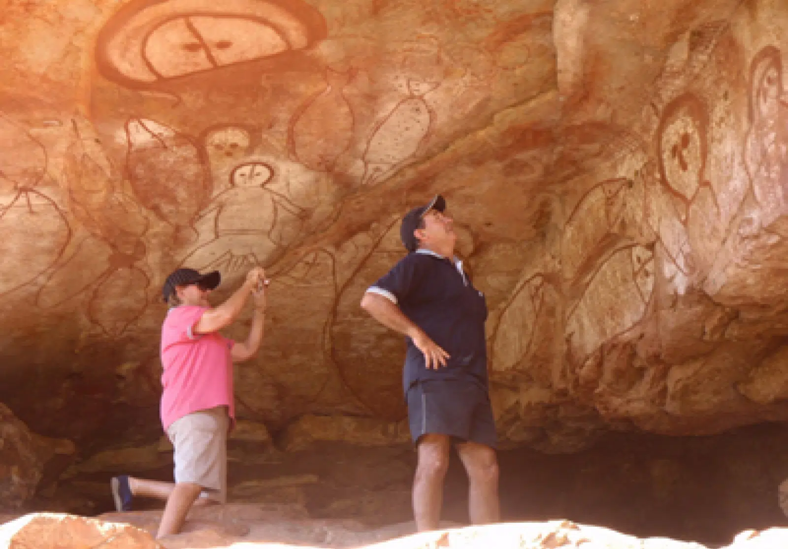 Two guests admire the Indigenous rock drawings and paintings in a cave in the Kimberley as part of their tour.