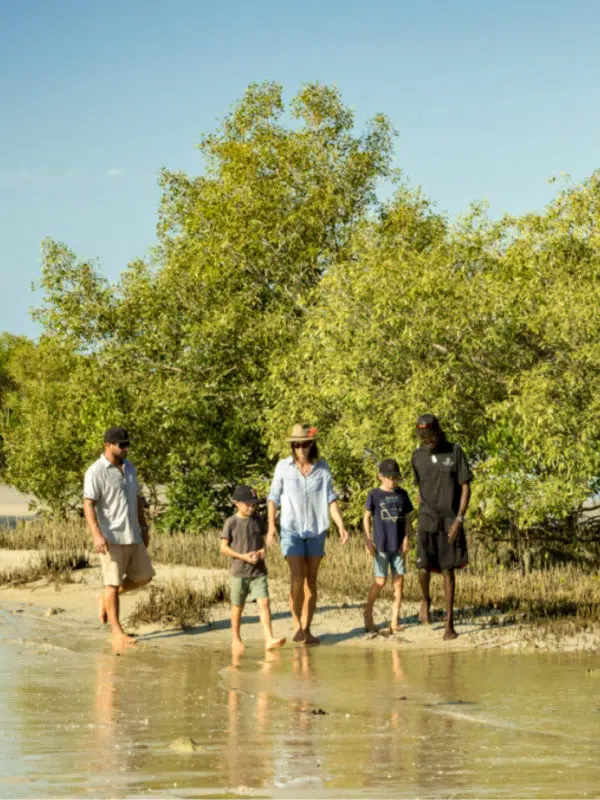 Terry Hunter walks alongside the Mangroves on a beach during his Borrgoron Cultural Tour. He talks to a group of guests, showing them the natural landscape and explaining the historical significance of Cygnet Bay to his culture and community.