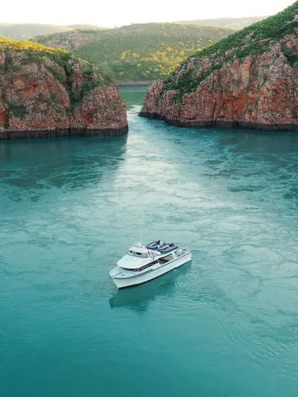 A boat sits on the calm, turquoise waters in the foreground, in front of the iconic Horizontal Falls. The Horizontal Falls are an unusual natural phenomenon on the coast of the Kimberley region in Western Australia, where tidal flows causes waterfalls on the ebb and flow of each tide.