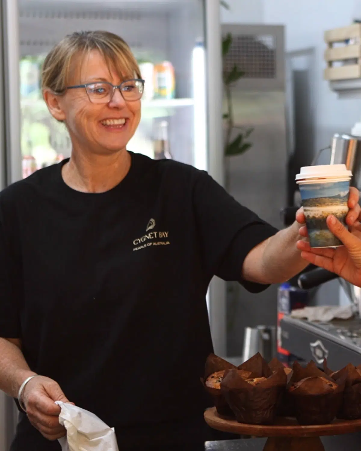 One of our friendly kiosk staff members smiles at a customer, handing them their coffee and muffin.