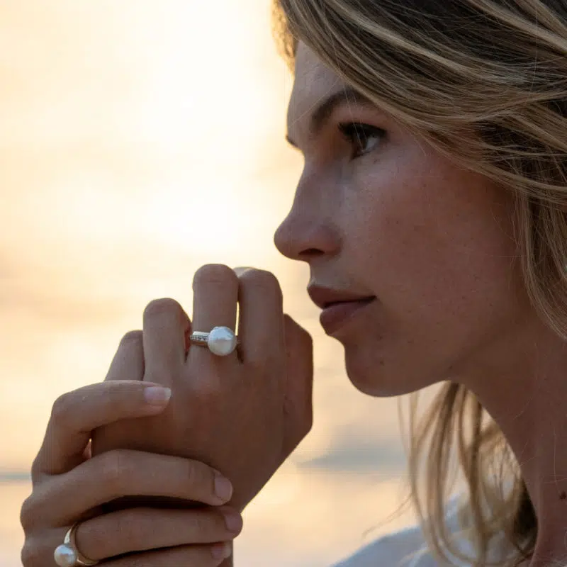 A model wears the Classics Pearl Jewellery Collection while enjoying the beautiful Kimberley sunrise. She wears a Mojo Ring with diamonds on her left hand and a Moji Ring without diamonds on her right. All featured pearls are Australian South Sea pearls locally grown at our Cygnet Bay Pearl Farm.