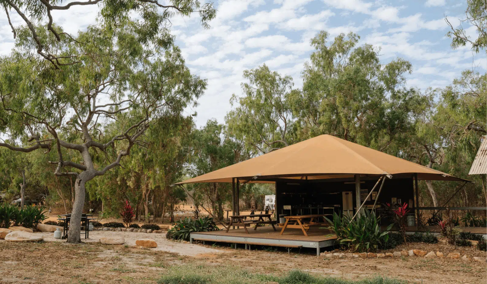 Our Pearler's Village Camping & Caravan site has a shared amenities area that is completely covered to provide shade for our guests. This space is surrounded by lush Australian shrubbery, tall trees, and grass. The amenities included in this particular space is a shared kitchen with a fridge, stove, sink, and food preparation area, as well as a bathroom for guests to use.