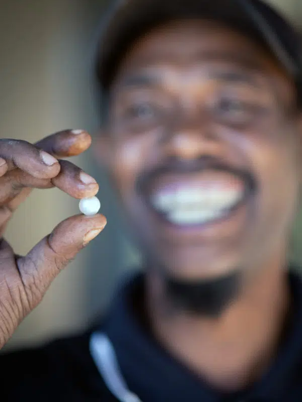 A lustrous, Australian South Sea pearl sits between the forefinger and thumb of Terry Hunter in the foreground, with his big smile blurry in the background, after just being harvested at our Cygnet Bay Pearl Farm where our Australian South Sea pearls are cultivated and harvested.