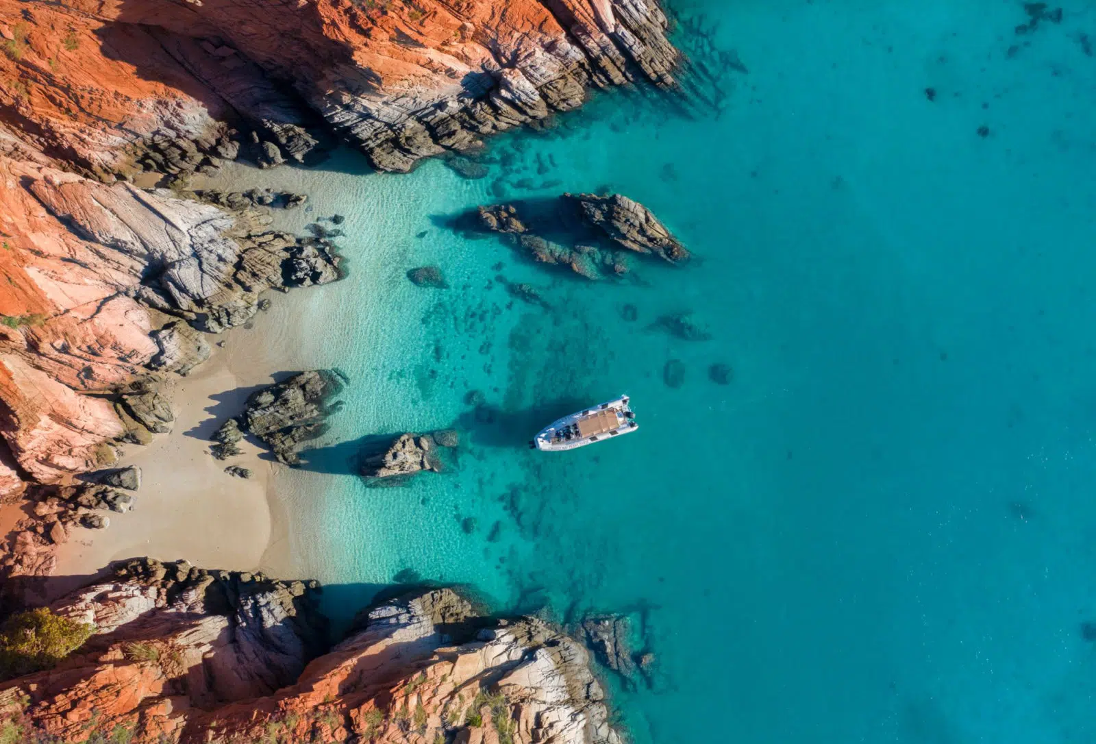 A beautiful aerial visual of a boat sitting on the calm sea, travelling towardsArchipelago Islands that are scattered along the coastline of the Dampier Peninsula, with turquoise blue waters that are almost crystal clear.Our Tours.